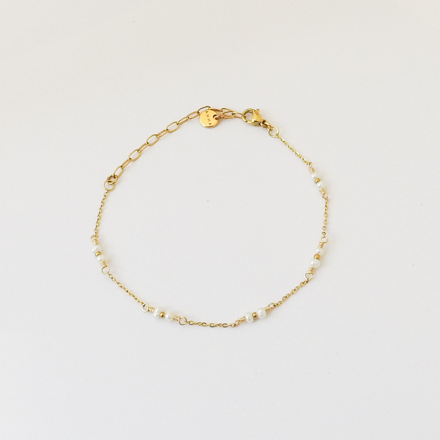 A delicate gold chain bracelet with small white beads spaced along the chain, displayed on a clean white background.