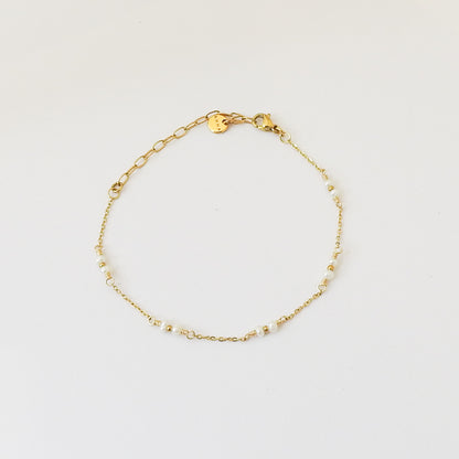 A delicate gold chain bracelet with small white beads spaced along the chain, displayed on a clean white background.