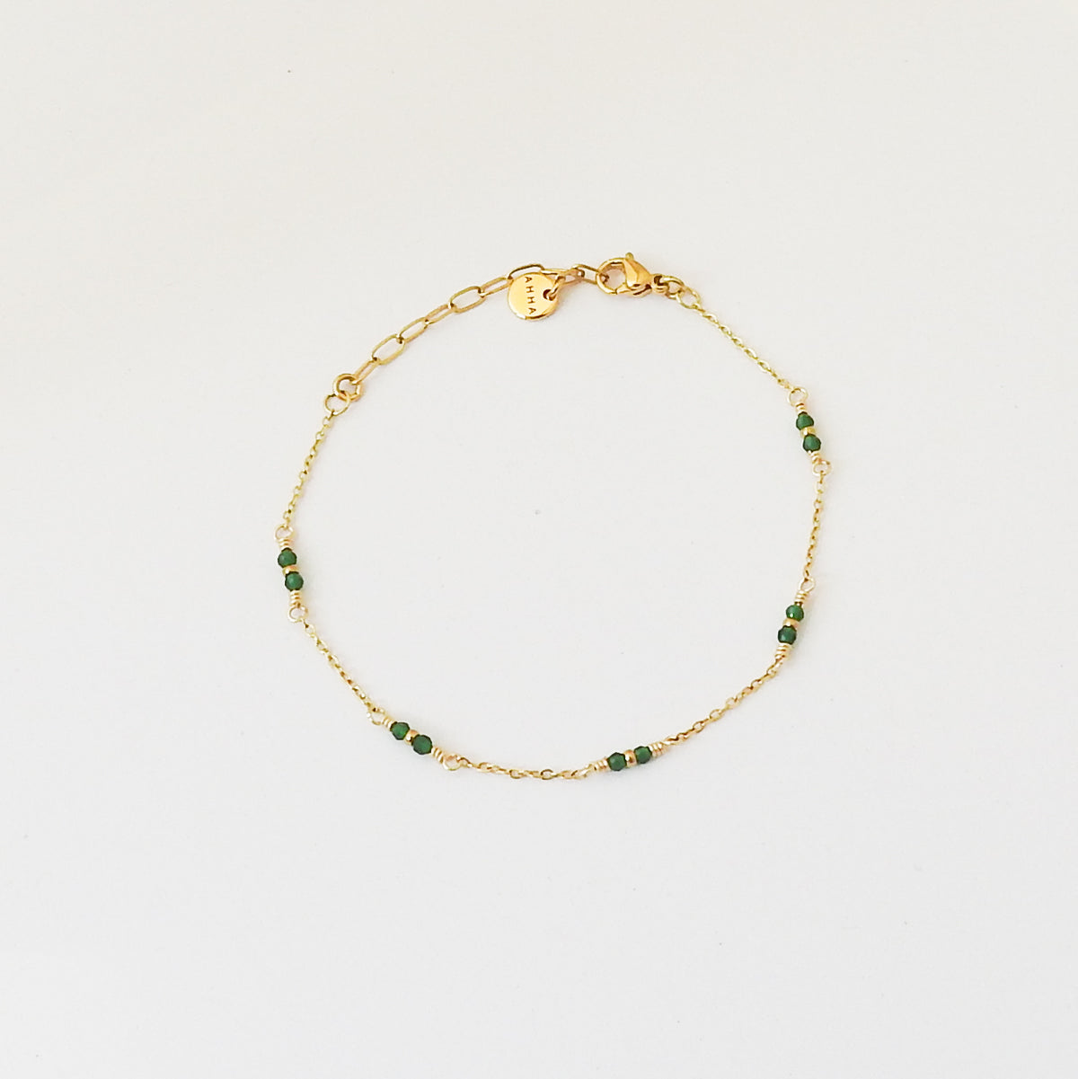 A delicate gold chain bracelet with small green faceted beads spaced along the chain, displayed on a clean white background.