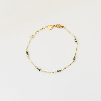 A delicate gold chain bracelet with small green faceted beads spaced along the chain, displayed on a clean white background.