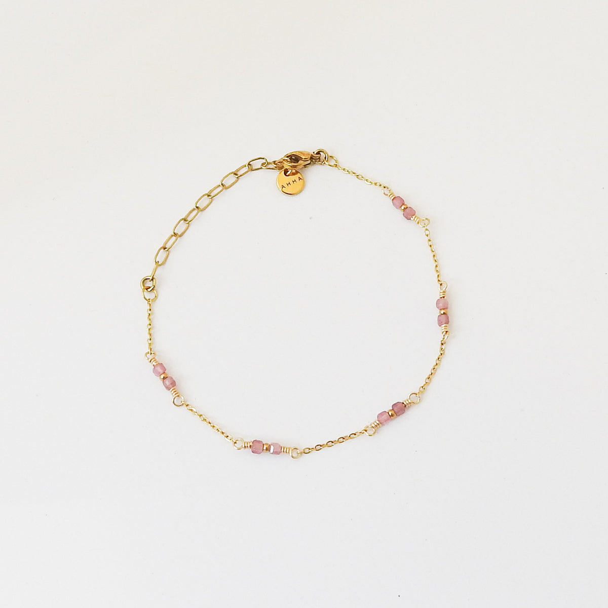 A delicate gold chain bracelet with small pink faceted beads spaced along the chain, displayed on a clean white background. A small gold tag is attached near the clasp.