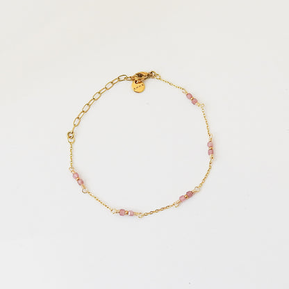 A delicate gold chain bracelet with small pink faceted beads spaced along the chain, displayed on a clean white background. A small gold tag is attached near the clasp.