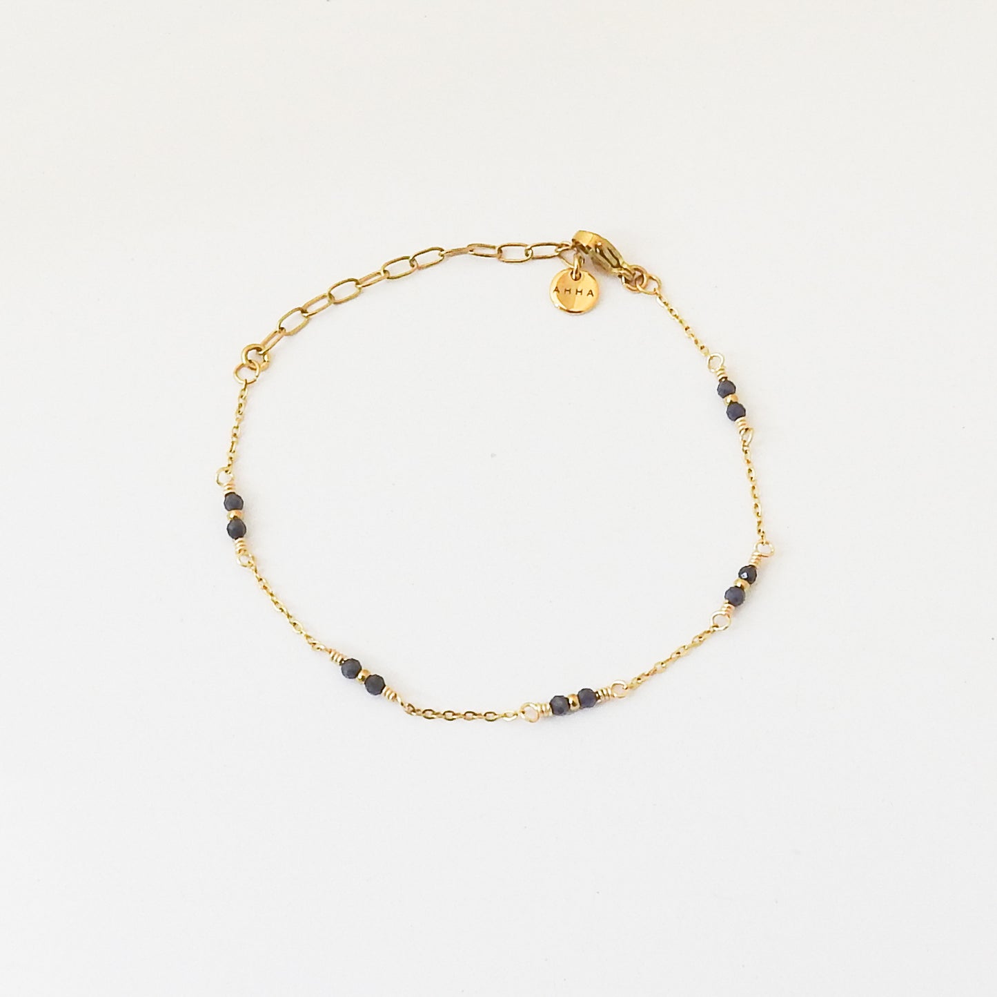 A delicate gold chain bracelet with small dark blue beads spaced along the chain, displayed on a clean white background.
