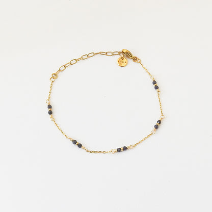 A delicate gold chain bracelet with small dark blue beads spaced along the chain, displayed on a clean white background.