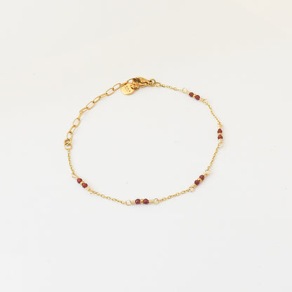 A delicate gold chain bracelet with small red beads spaced along the band, displayed on a clean white background.
