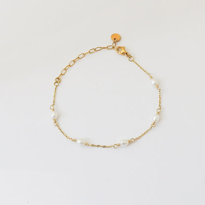 A delicate gold chain bracelet with irregular white pearl beads spaced along the chain, displayed on a clean white background.