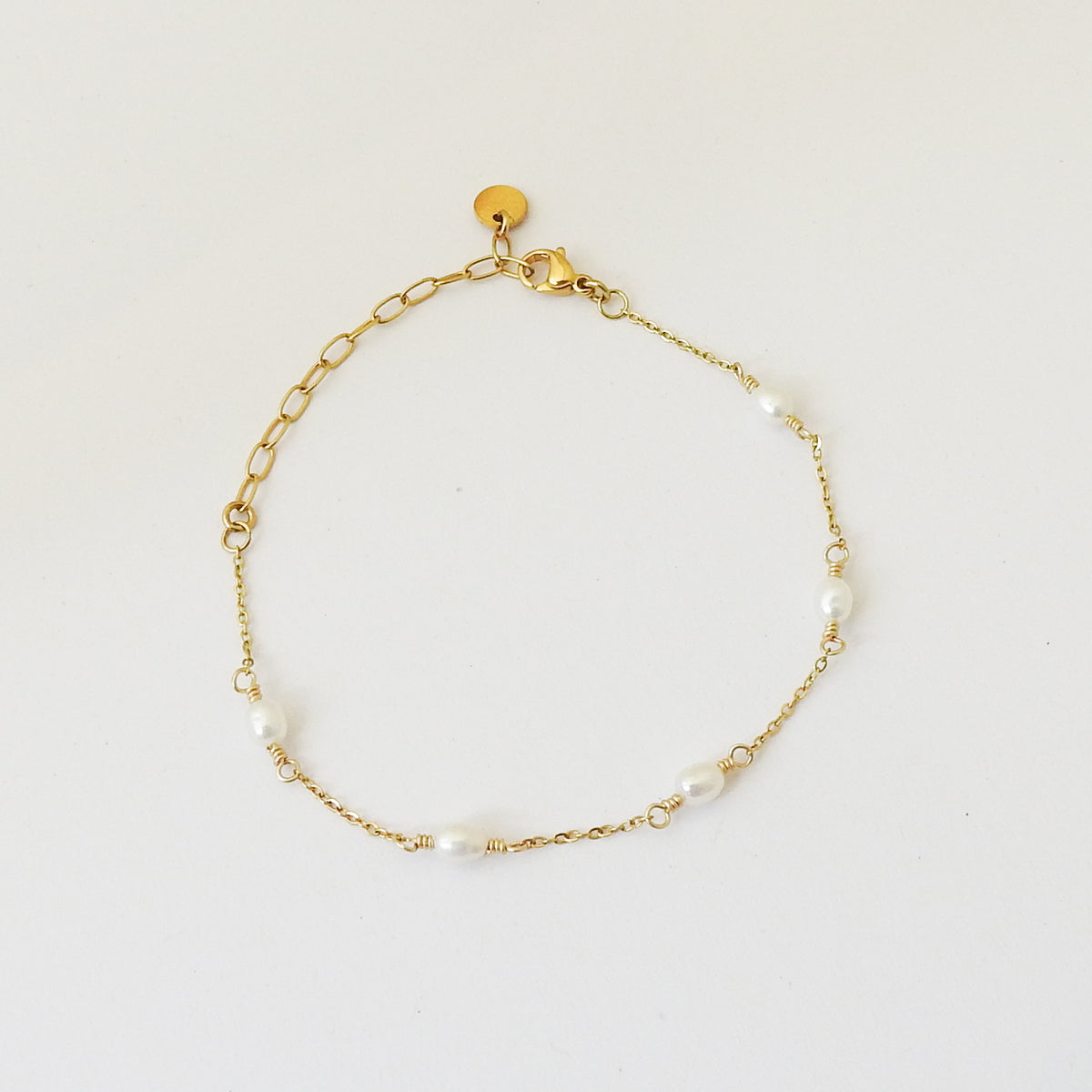 A delicate gold chain bracelet with small white pearl beads spaced along the chain, displayed on a clean white background.