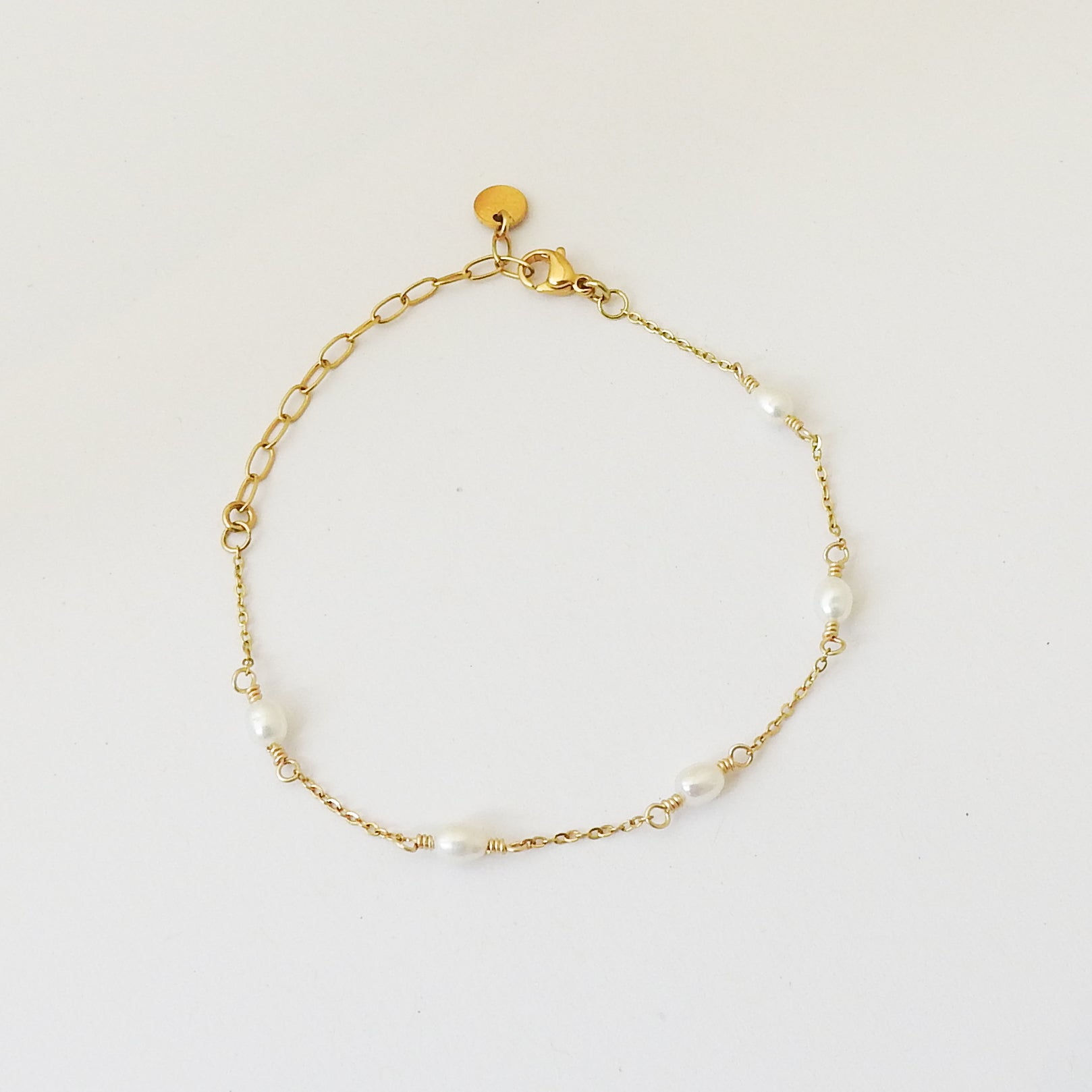 A delicate gold chain bracelet with small white pearl beads spaced along the chain, displayed on a clean white background.