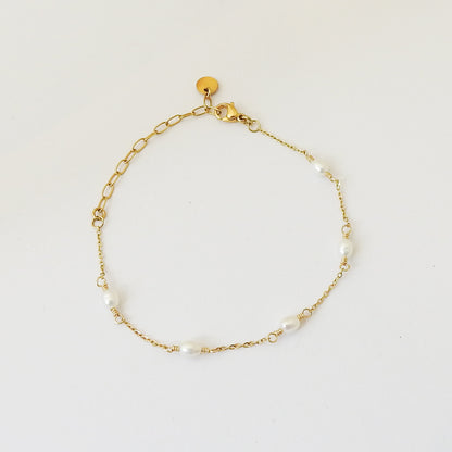 A delicate gold chain bracelet with small white pearl beads spaced along the chain, displayed on a clean white background.