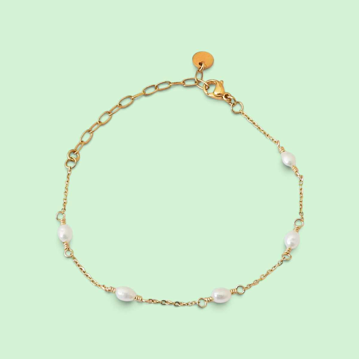 A delicate gold chain bracelet with five small white baroque pearls spaced along the chain, displayed on a solid pale green background.