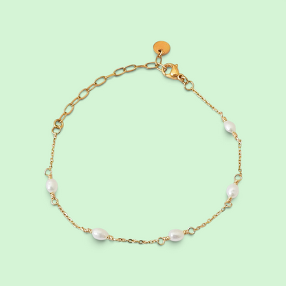 A delicate gold chain bracelet with five small white baroque pearls spaced along the chain, displayed on a solid pale green background.