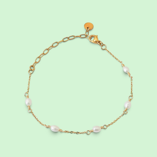 A delicate gold chain bracelet with five small white baroque pearls spaced along the chain, displayed on a solid pale green background.