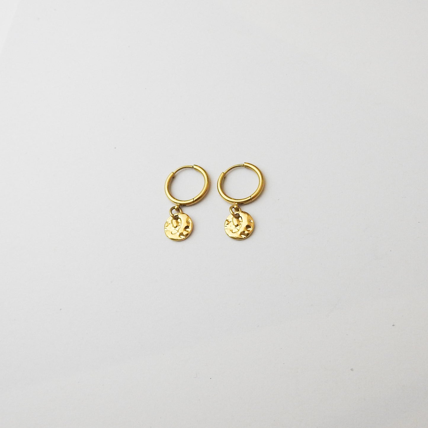 A pair of small gold hoop earrings with dangling textured round charms, displayed on a clean white background.
