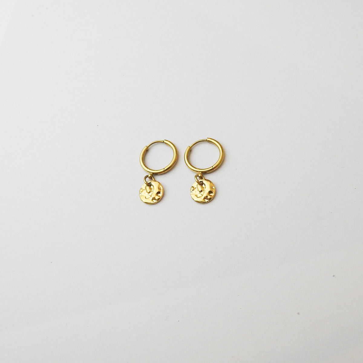 A pair of small gold hoop earrings with dangling textured round charms, displayed on a clean white background.
