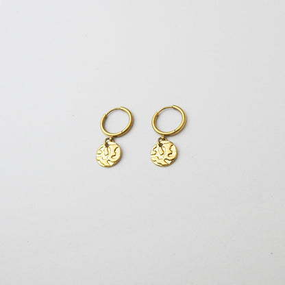 A pair of small gold huggie hoop earrings with dangling textured round charms, displayed on a clean white background.