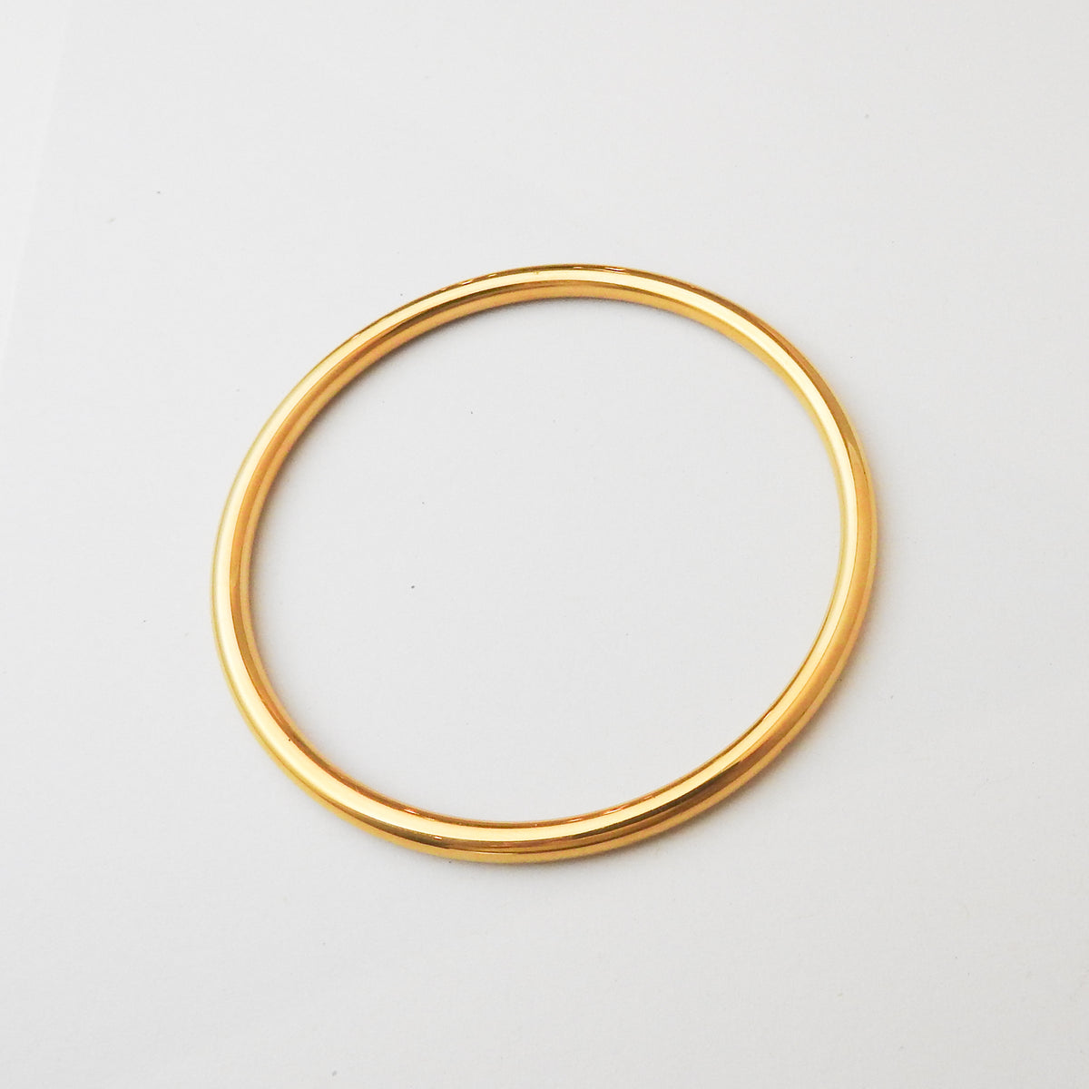 A polished gold-colored metal bangle bracelet, shown from a top-down view on a clean white background.