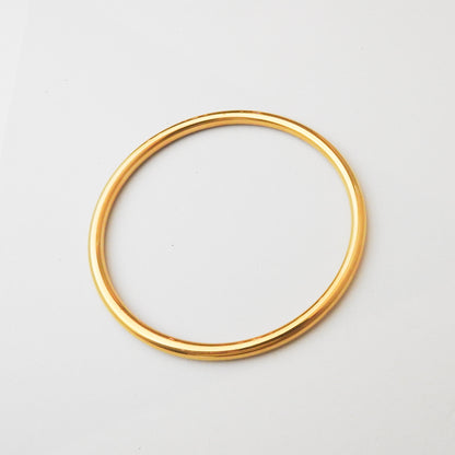 A polished gold-colored metal bangle bracelet, shown from a top-down view on a clean white background.