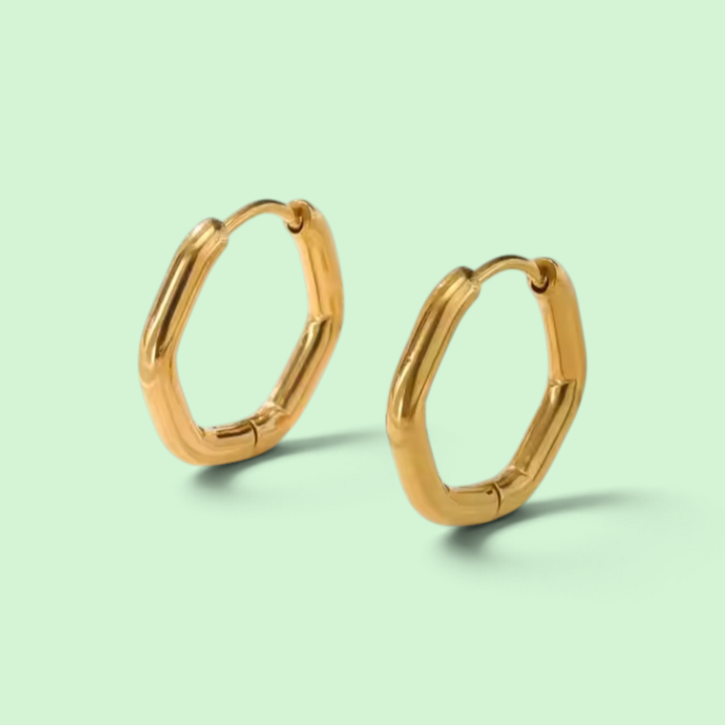 A pair of gold-toned, irregularly shaped hoop earrings on a solid pale mint green background.