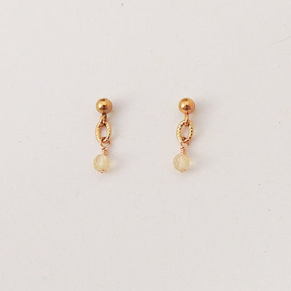 A pair of gold-toned dangle earrings with a small round bead, textured oval link, and faceted clear crystal drop, shown on a plain light background.