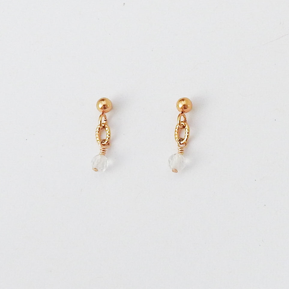 A pair of gold dangle earrings with a small clear faceted bead hanging from an openwork oval loop, shown on a plain white background.