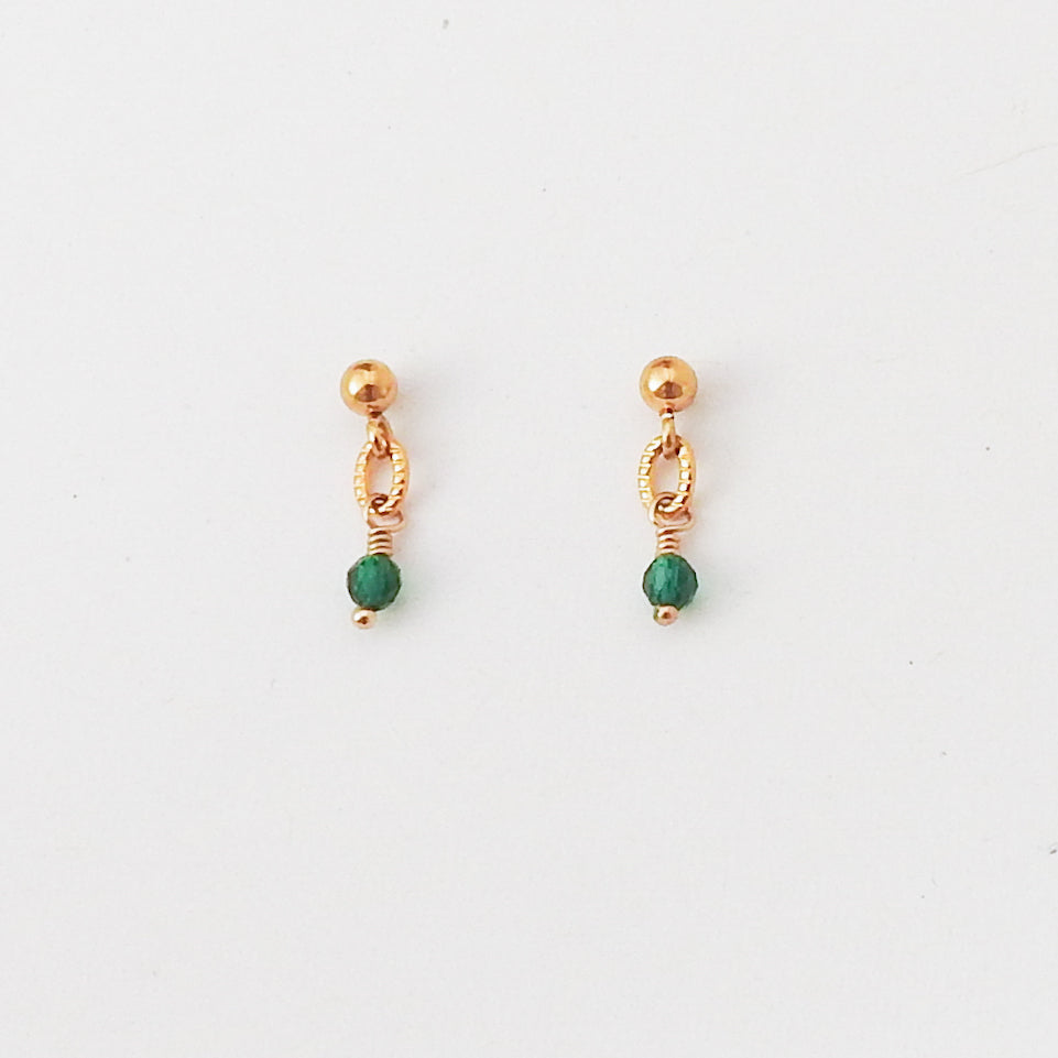A pair of small gold-toned dangle earrings with a faceted green bead at the bottom, shown on a plain white background.
