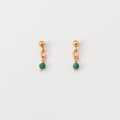 A pair of small gold-toned dangle earrings with a faceted green bead at the bottom, shown on a plain white background.