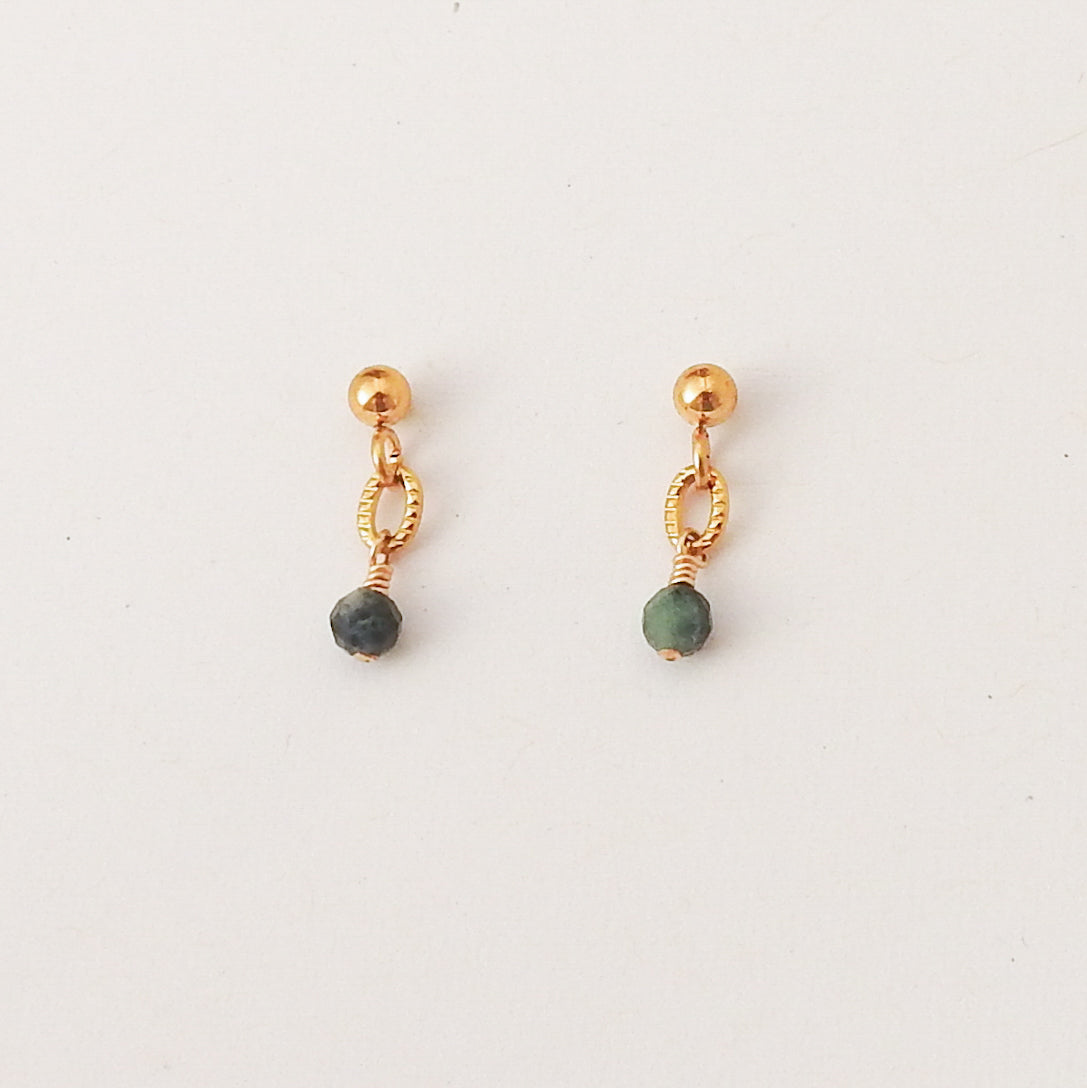 A pair of gold dangle earrings with a small green bead hanging from a twisted wire loop, shown on a plain white background.