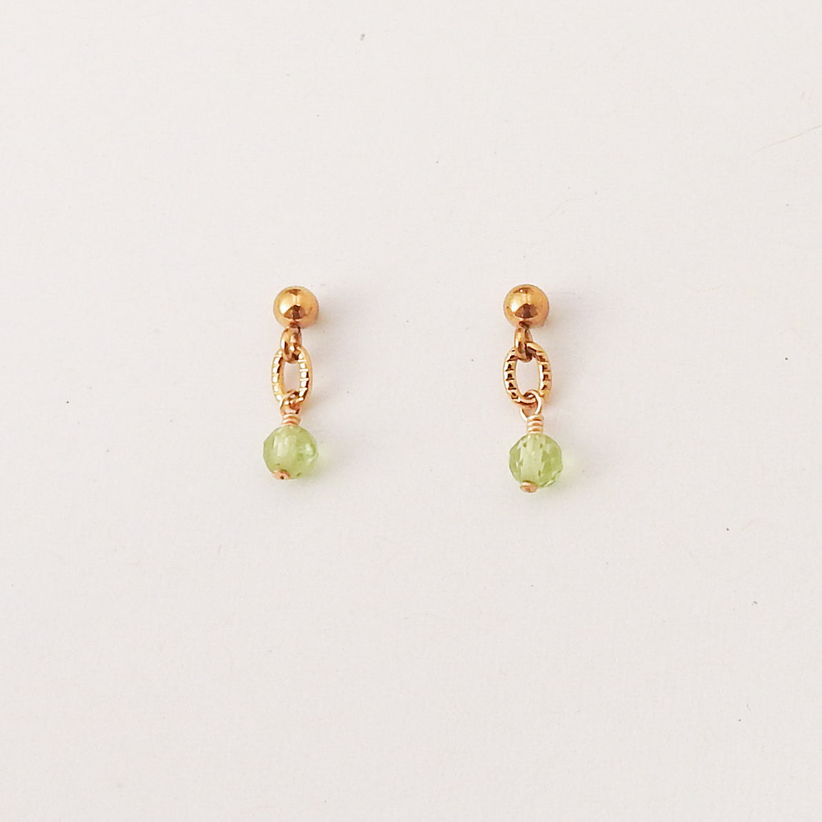 A pair of small gold dangle earrings with a faceted light green bead hanging from a delicate openwork loop, shown on a plain white background.