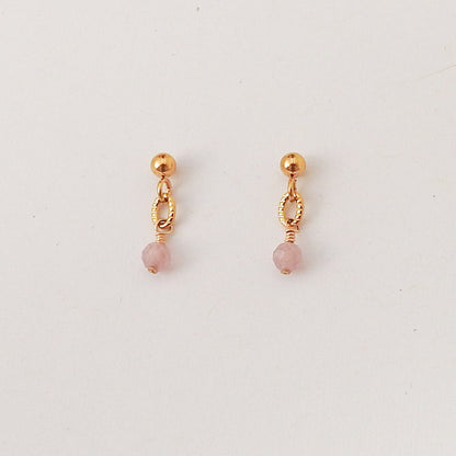 A pair of small gold dangle earrings with a faceted pink bead hanging from a textured oval link, displayed on a clean white background.