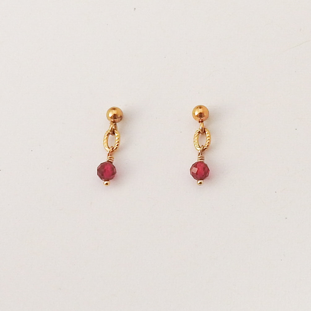 A pair of gold dangle earrings with faceted red gemstone drops, displayed on a clean white background.