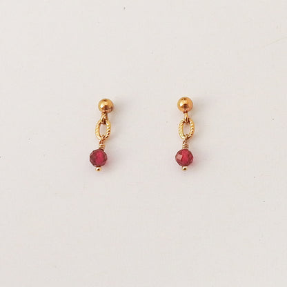 A pair of gold dangle earrings with faceted red gemstone drops, displayed on a clean white background.