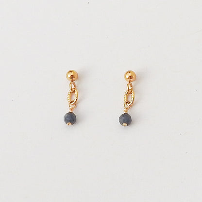 A pair of gold dangle earrings with a small gold ball, a twisted gold chain link, and a faceted dark gray bead dangling at the bottom, shown on a plain white background.