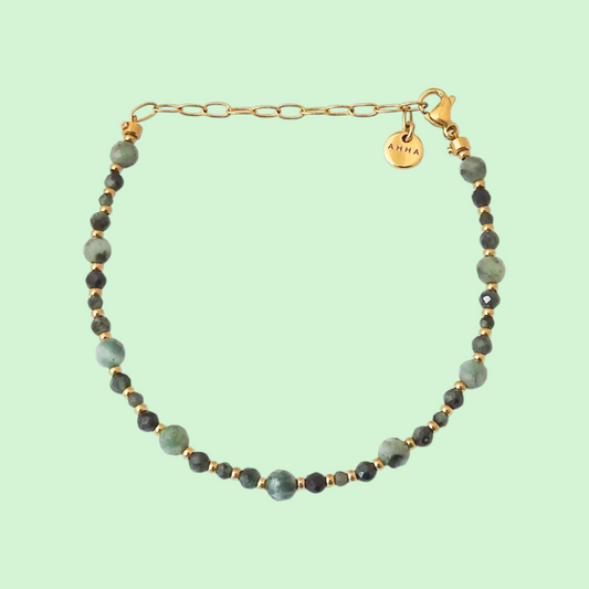 A beaded bracelet with light green and dark green faceted beads separated by small gold spacer beads, featuring a gold chain extender and a round gold charm engraved with AHHA