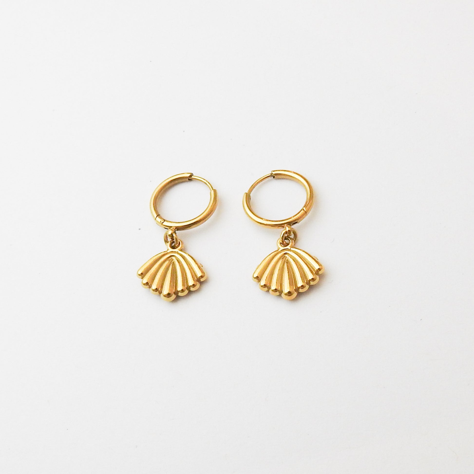 A pair of gold hoop earrings with dangling scallop-shaped charms, displayed on a clean white background.