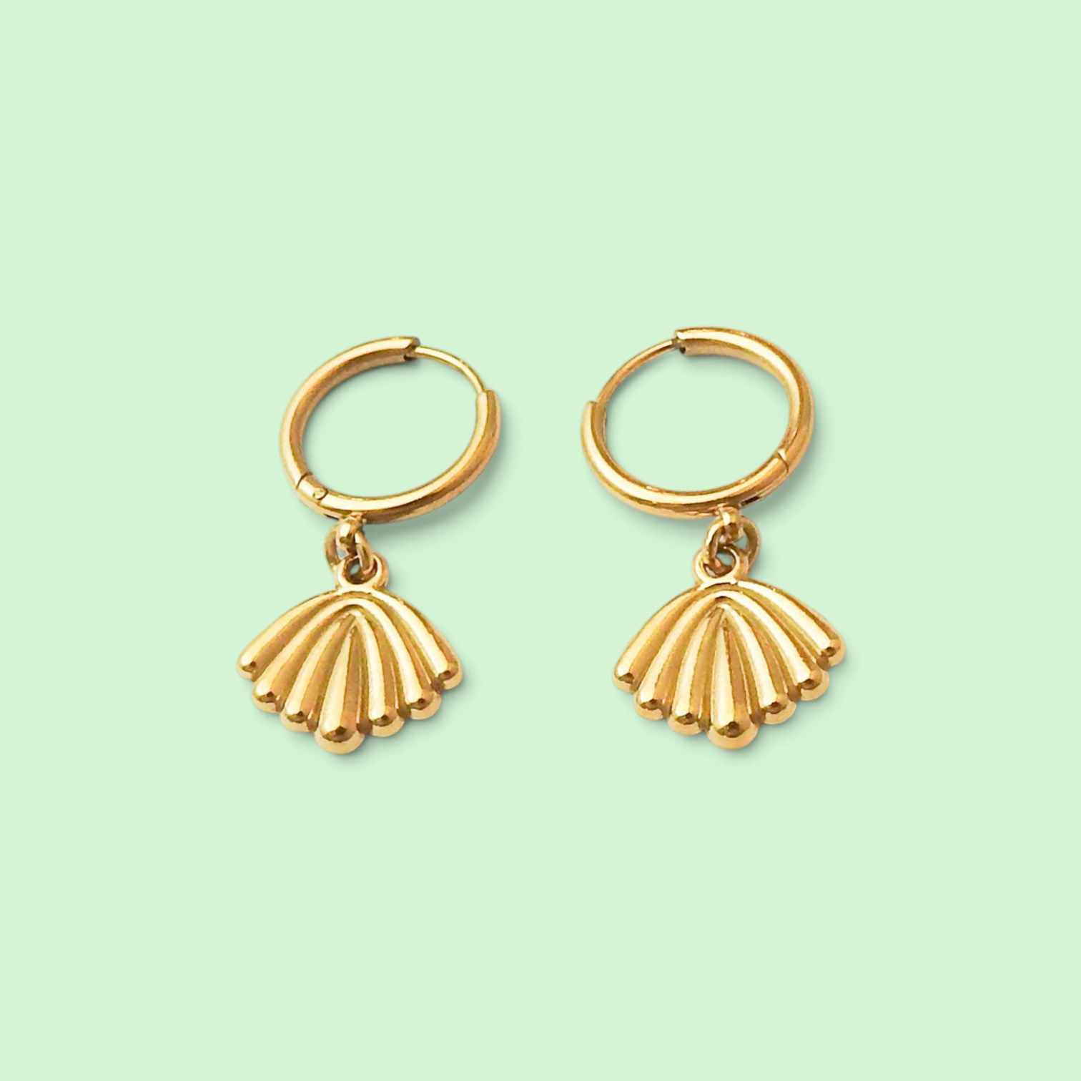 A pair of gold hoop earrings with dangling fan-shaped seashell charms, displayed on a solid pale mint green background.