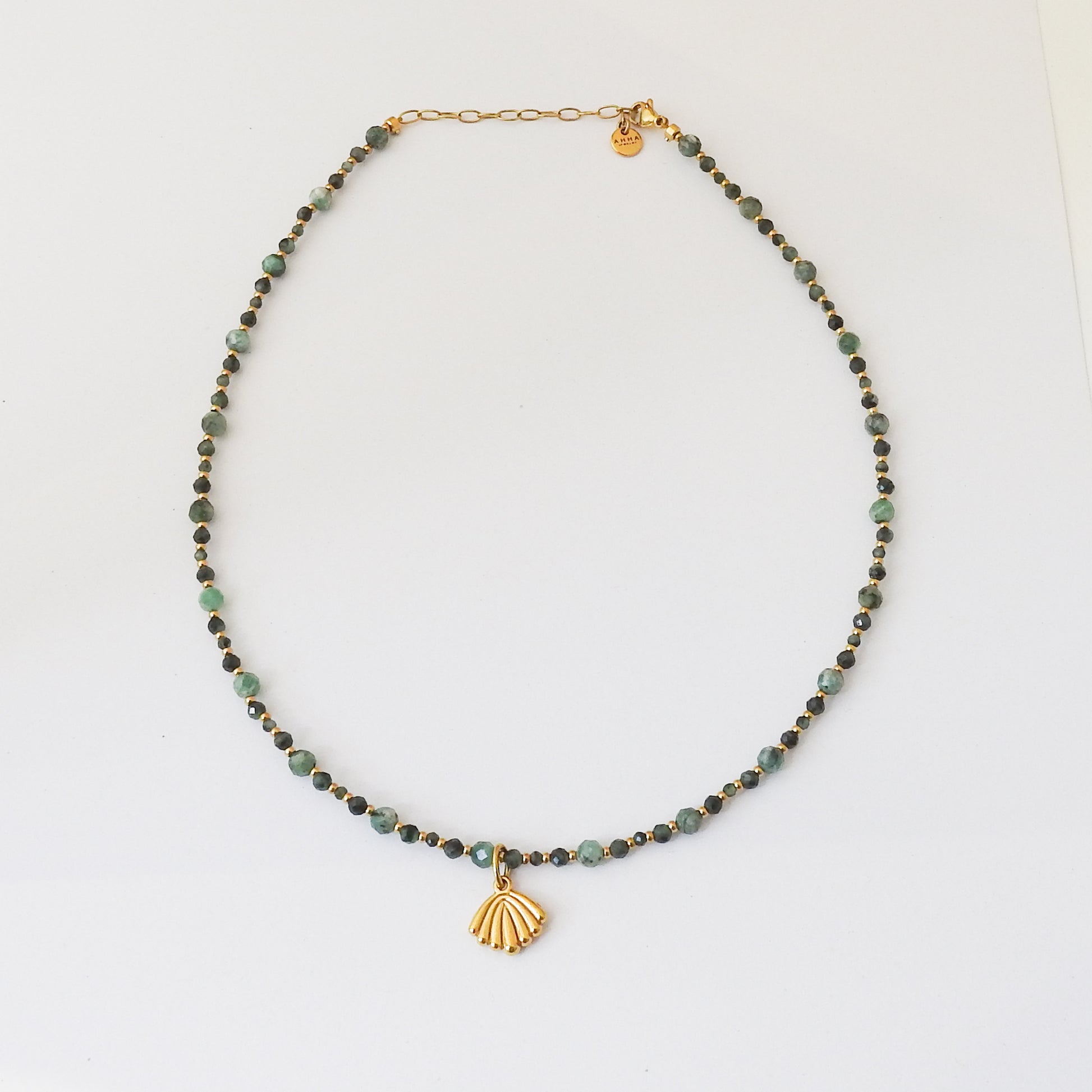 A beaded necklace featuring small green and dark green beads with a gold-tone clasp and a gold-tone shell-shaped pendant, displayed on a clean white background.