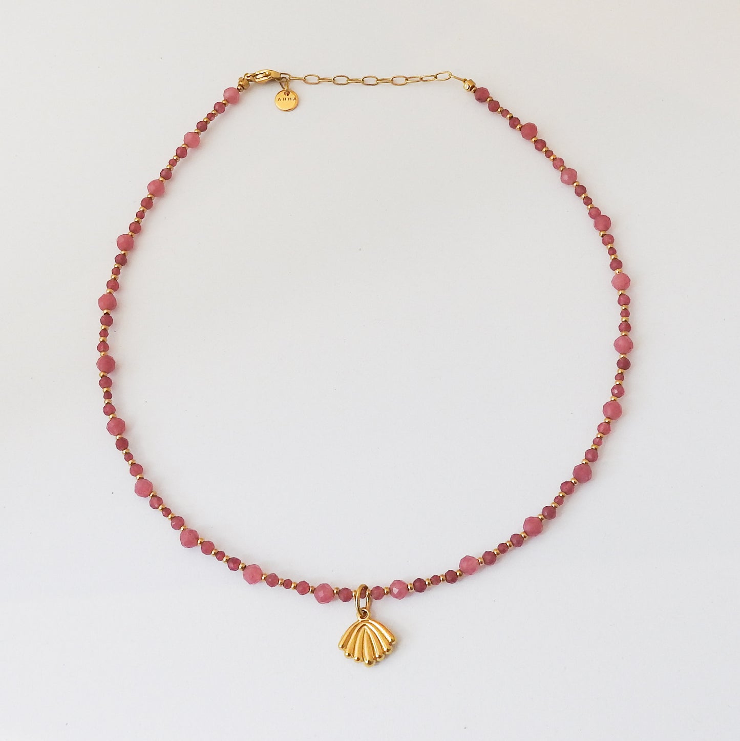 A beaded necklace featuring faceted pinkish-red beads and a gold shell pendant, displayed on a clean white background.