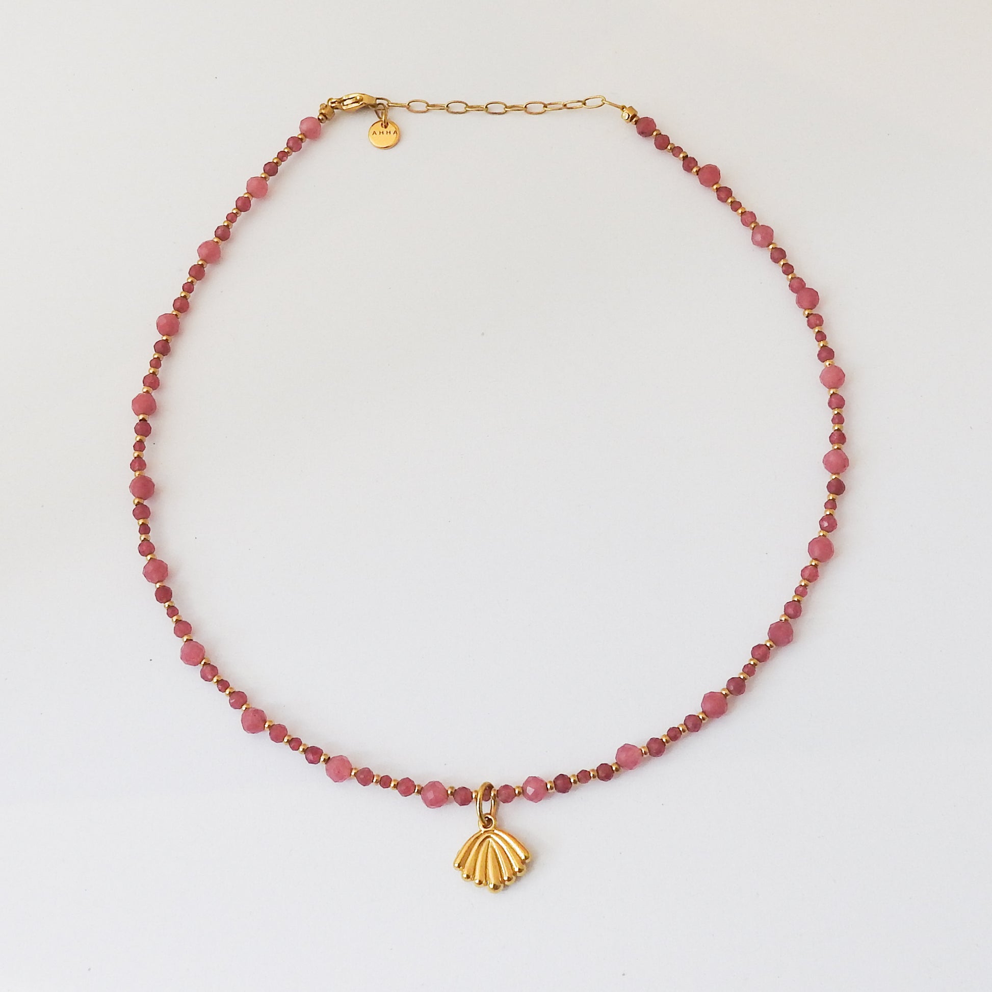 A beaded necklace featuring faceted pinkish-red beads and a gold shell pendant, displayed on a clean white background.