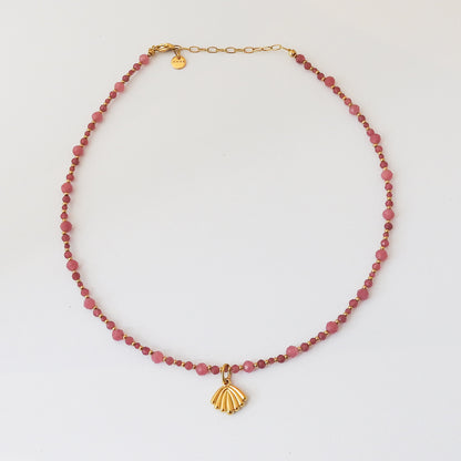 A beaded necklace featuring faceted pinkish-red beads and a gold shell pendant, displayed on a clean white background.