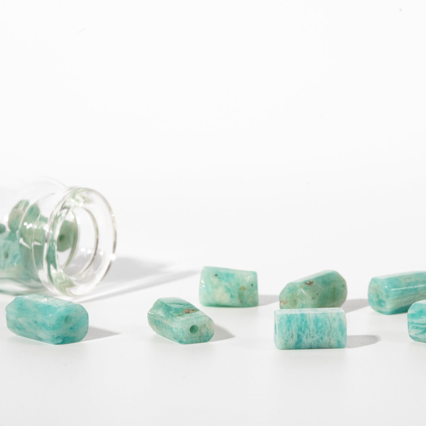 Turquoise rectangular gemstone beads with rounded ends, some lying on a white surface and one inside a clear glass jar, photographed on a clean white background.