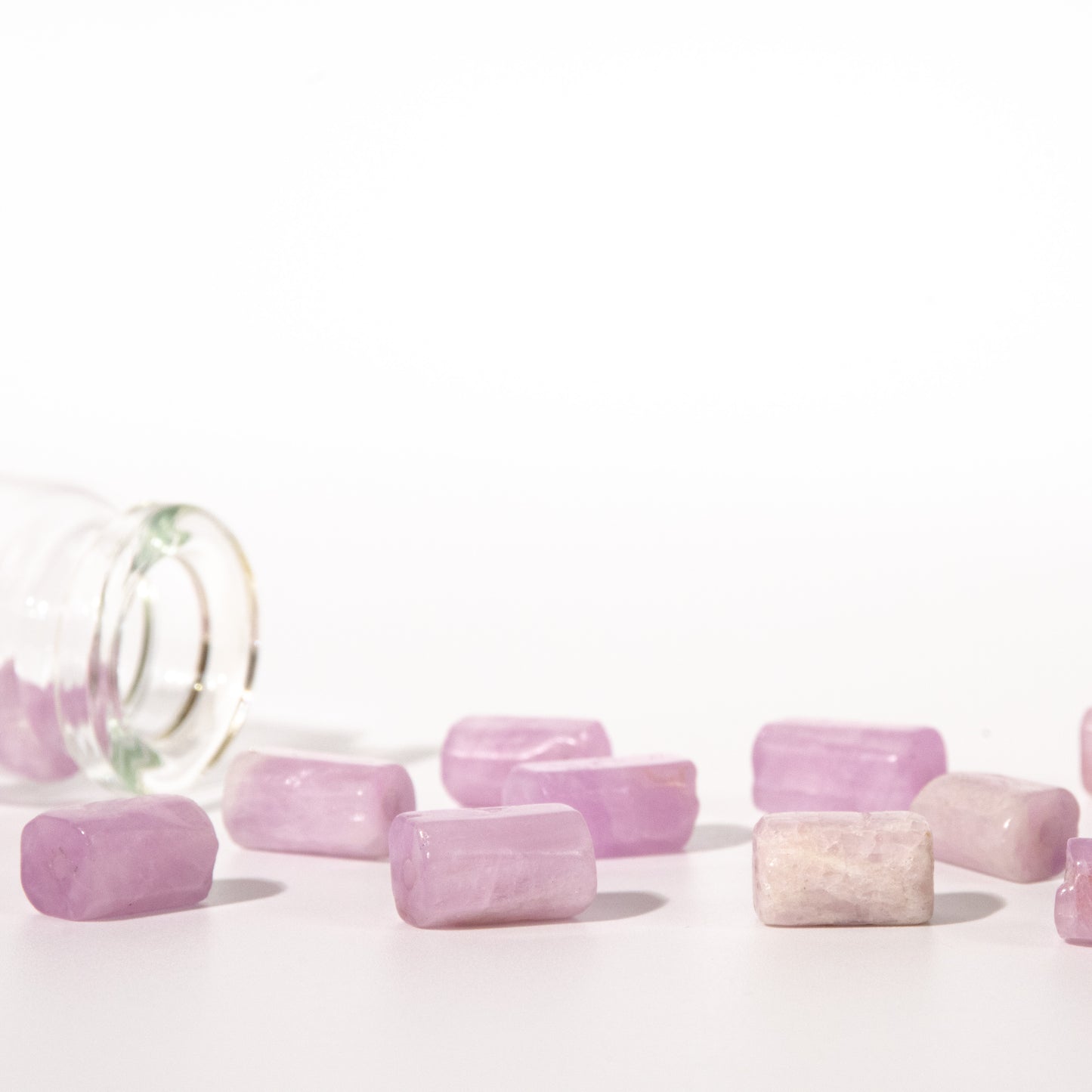 Several small lavender-pink rectangular stone tablets scattered on a white surface, with a tipped-over clear glass bottle on the left.