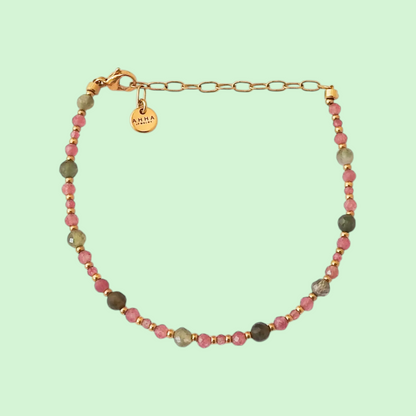 A beaded necklace with alternating pink and dark red beads, featuring a gold-tone shell-shaped charm at the center and a gold clasp, displayed on a solid pale mint green background.