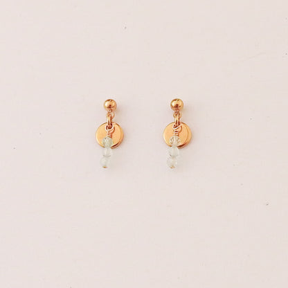 A pair of small rose gold dangle earrings with a flat circular disc, a wrapped bead, and a tiny light blue bead drop, shown on a plain off-white background.