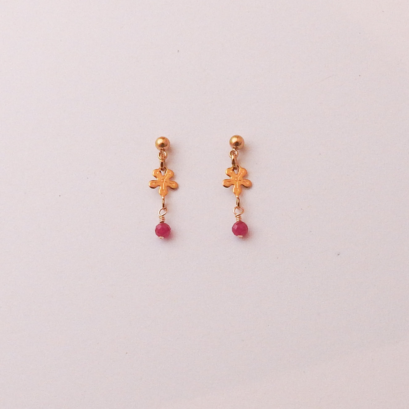 A pair of gold-toned dangle earrings with small floral charms and pink bead drops, displayed on a plain light background.