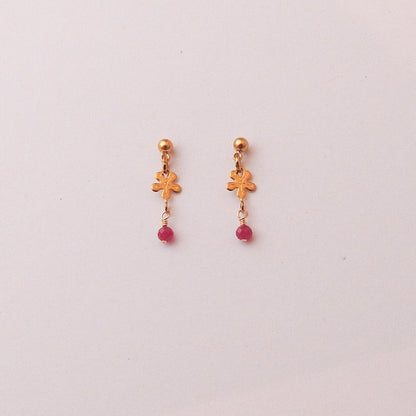 A pair of gold-toned dangle earrings with small floral charms and pink bead drops, displayed on a plain light background.
