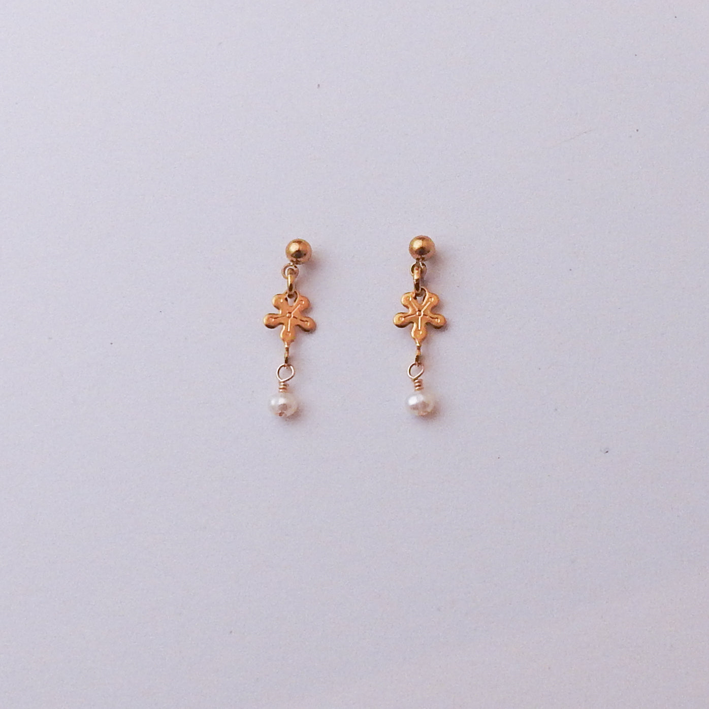 A pair of gold-toned dangle earrings with small floral charms and white pearl drops, displayed on a light gray background.