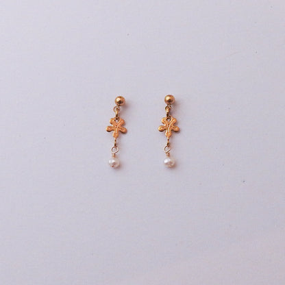 A pair of gold-toned dangle earrings with small floral charms and white pearl drops, displayed on a light gray background.