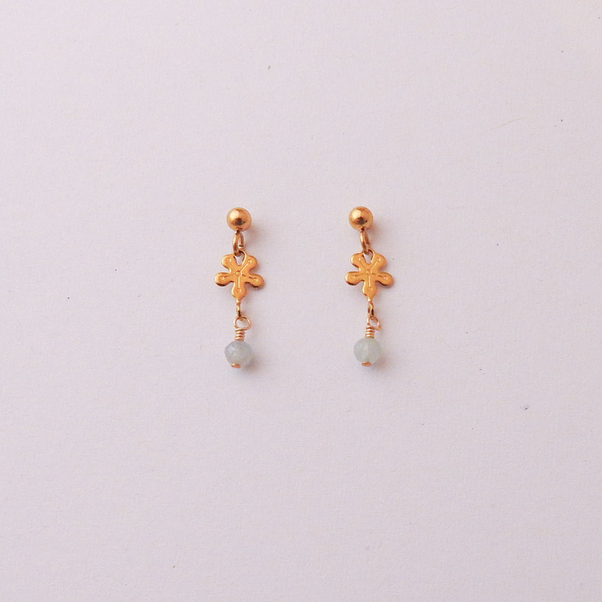 A pair of gold dangle earrings with a textured leaf charm and a small light blue bead drop, displayed on a plain off-white background.