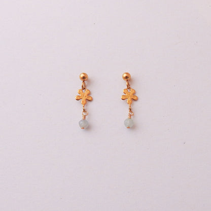 A pair of gold dangle earrings with a textured leaf charm and a small light blue bead drop, displayed on a plain off-white background.