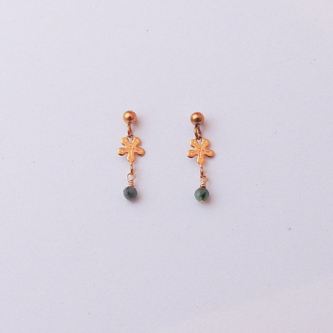 A pair of small gold-toned dangle earrings with a flower-shaped charm and a green bead drop, shown on a plain light background.